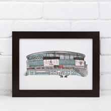 Load image into Gallery viewer, A framed print of the Emirates Stadium, showing the front of the Arsenal FC ground. The print is in a white frame against a white brick wall, on a white table.
