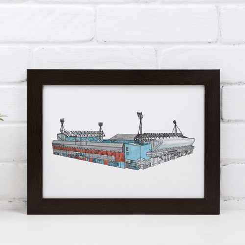 A framed print of Portman Road, home to Ipswich Town FC. Framed in a black frame, photographed against a white brick wall.