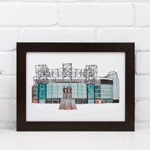 Load image into Gallery viewer, A detailed Old Trafford art print, the piece shows the front of the football stadium home to Manchester United FC. Framed in a black frame and propped against a white brick wall.
