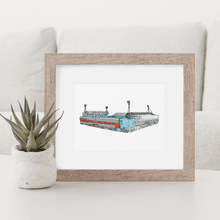 Load image into Gallery viewer, A print of Ipswich Town Football Club, the print shows the Cobbold stand and the Sir Bobby Robson stand. It is photographed in a wooden frame on a coffee table.
