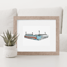 Load image into Gallery viewer, A print of Ipswich Town Football Club, the print shows the Cobbold stand and the Sir Bobby Robson stand. It is photographed in a wooden frame on a coffee table.