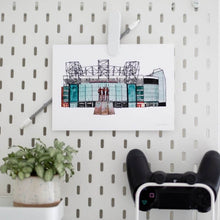 Load image into Gallery viewer, Manchester United wall art print of the Old Trafford ground. The piece is on a white peg board with a games console controller and a shelf with a small pot plant.