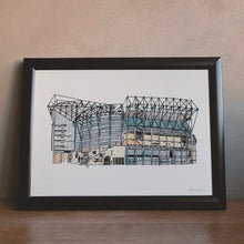 Load image into Gallery viewer, A framed pen and watercolour Newcastle United Print. The piece is in a simple black frame sat on a wooden table, against a pale pink plaster wall.