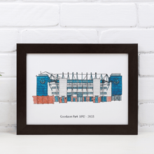 Load image into Gallery viewer, A personalised Everton football ground print, with the words 'Goodison Park 1892-2023' printed underneath. It is in a white frame against a white brick wall.