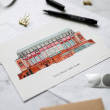 Load image into Gallery viewer, A personalised Liverpool FC print with 'You'll Never Walk Alone' printed underneath the painting. The piece is on a desk with a pen beside it.