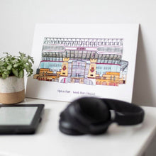 Load image into Gallery viewer, West Ham United wall art by Jessica Sian, a detailed illustration of the Upton Park football stadium. The piece is on a bedside table with headphones, a kindle and a small pot plant.