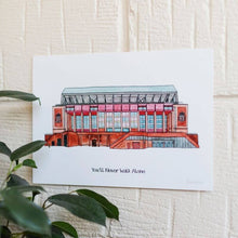Load image into Gallery viewer, A Liverpool FC Print of the club&#39;s football stadium. It shows a painted image of Anfield. The piece is displayed on a white brick wall with a plant in the lower left corner. 

