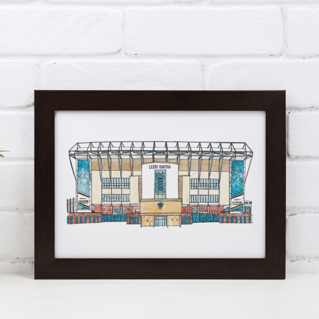 A piece of Leeds United wall art. The artwork is a fineliner and watercolour print of the artist's hand drawn piece. It's photographed in a black frame against a white brick wall.