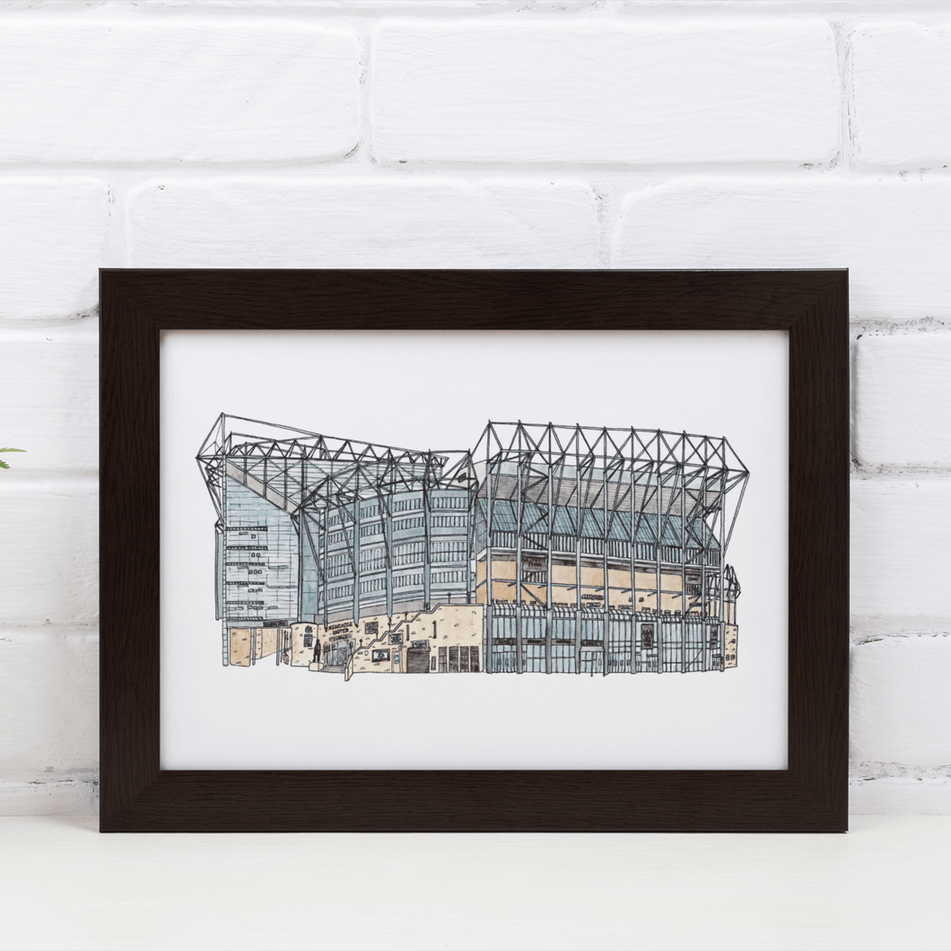 Newcastle United Football Stadium print, a detailed illustration of St James' Park hand drawn and painted by the artist Jessica Sian. The piece is in a black frame against a white brick wall.