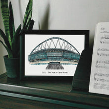 Load image into Gallery viewer, A detailed pen and watercolour illustration of Wembley Stadium with the text &#39;2022 - The Year It Came Home&#39; printed underneath. The piece is in a black frame, sat on a piano top next to a plant.
