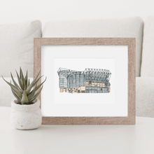 Load image into Gallery viewer, A Newcastle United football stadium print, the print shows St. James&#39; Park, home to Newcastle United F.C. It&#39;s in a white frame, on a white coffee table.
