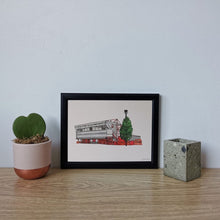 Load image into Gallery viewer, A hand drawn and painted print of Nottingham Forest Football Ground. The illustration is framed in a blacck frame, photographed on a desk next to a small pot plant.

